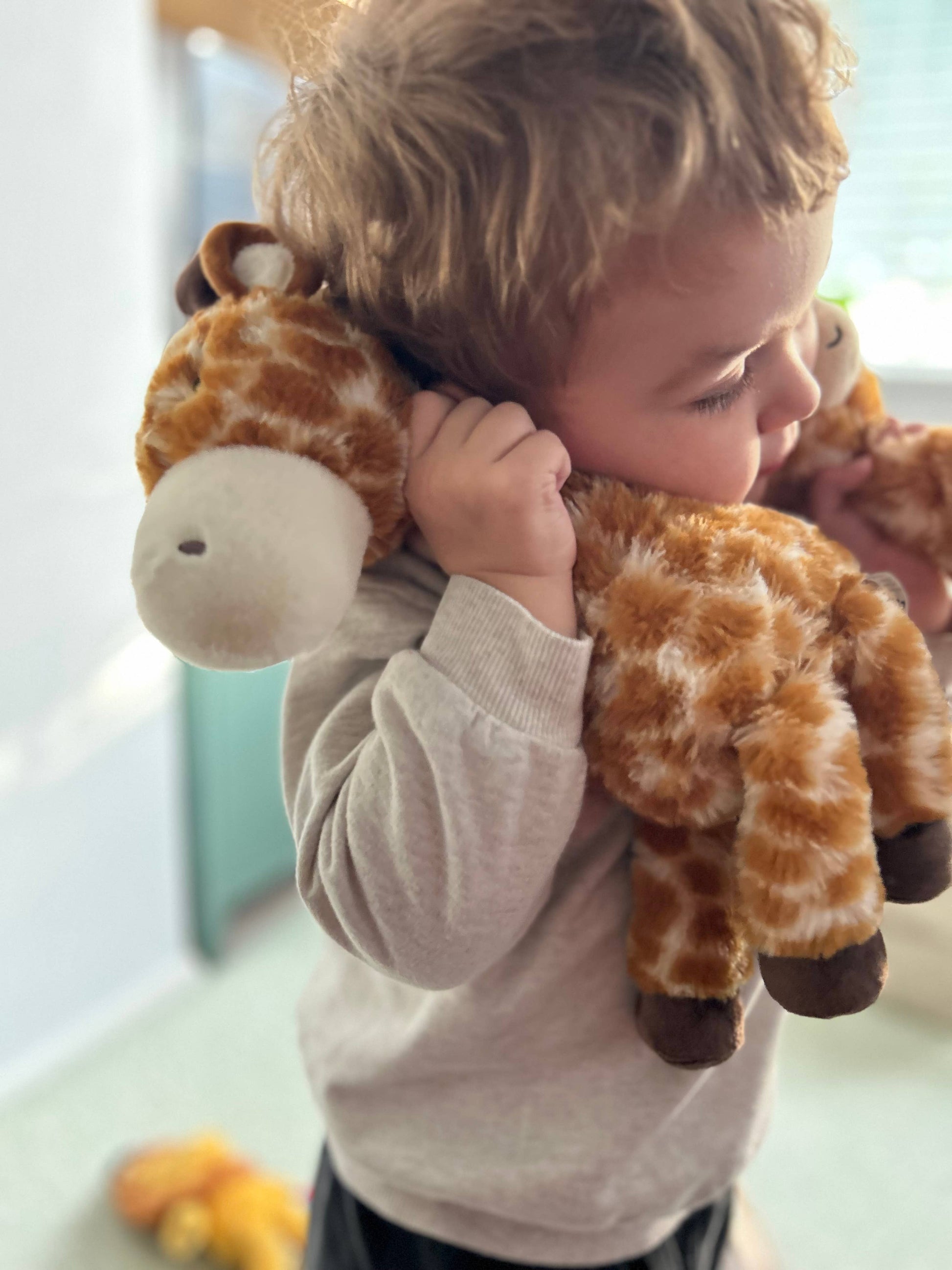 Child holding a plush giraffe toy indoors
