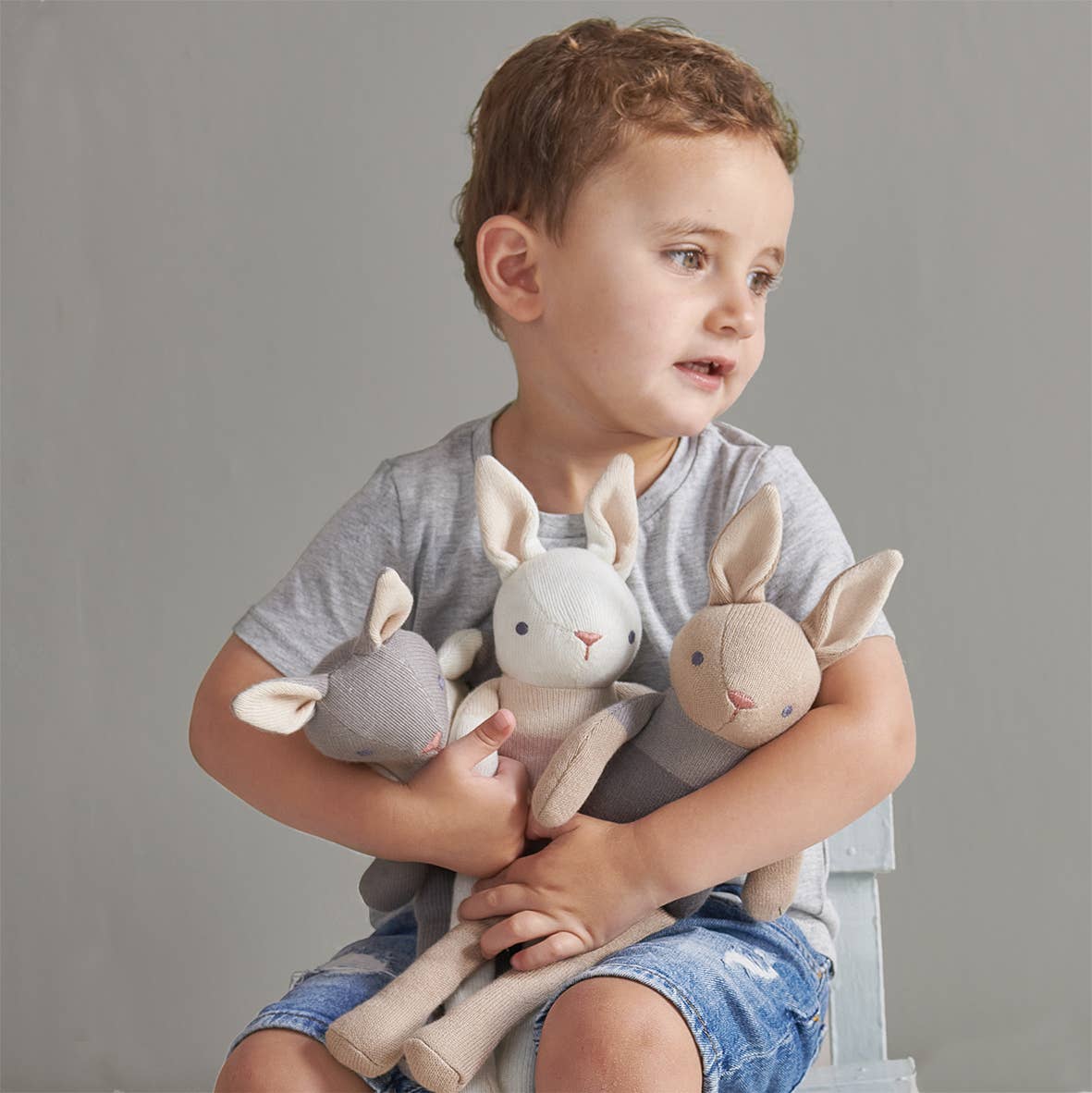 Child holding plush toys against a gray background