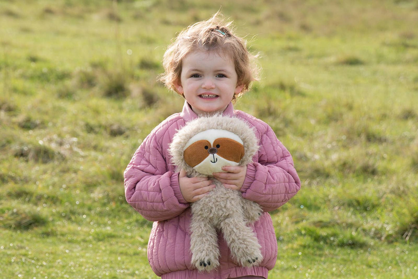 Child holding a stuffed sloth toy in an open field