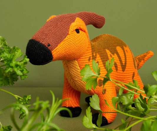 Knitted plush toy resembling a parasaurolophus dinosaur in orange with a crest, made from acrylic yarn with recycled polyester fill.