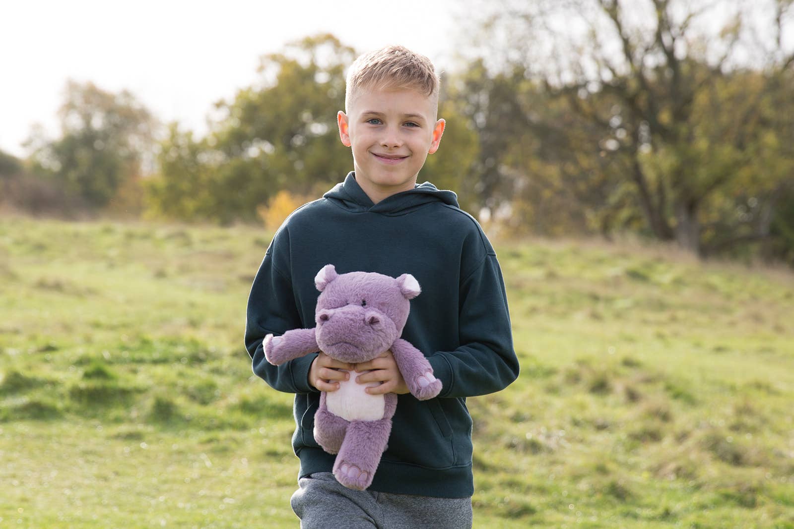 Young boy holding a purple hippo  in an outdoor setting