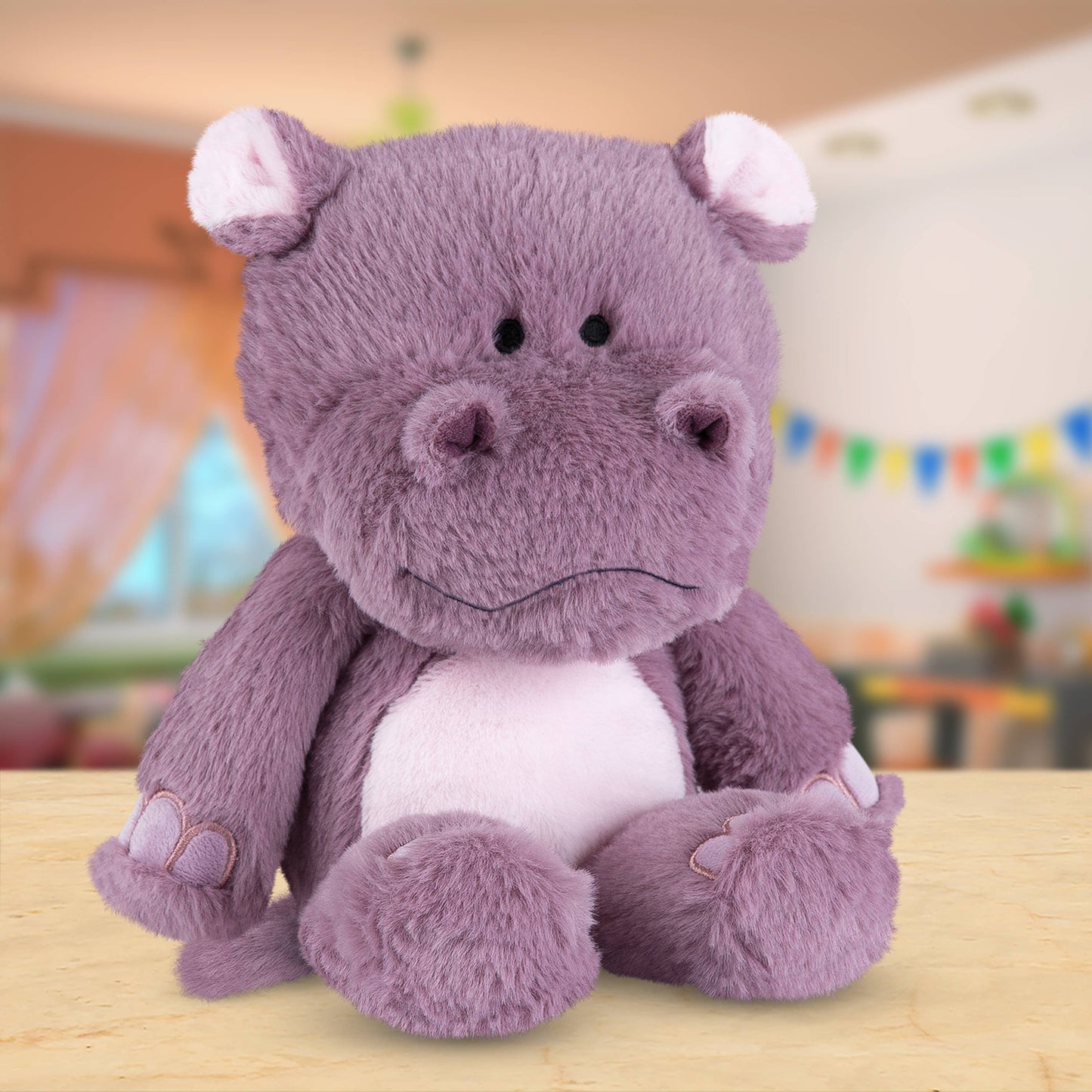 Purple plush toy hippo on a wooden surface with a blurred colorful background