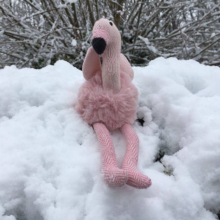 Knitted flamingo toy in the snow with a snowy background