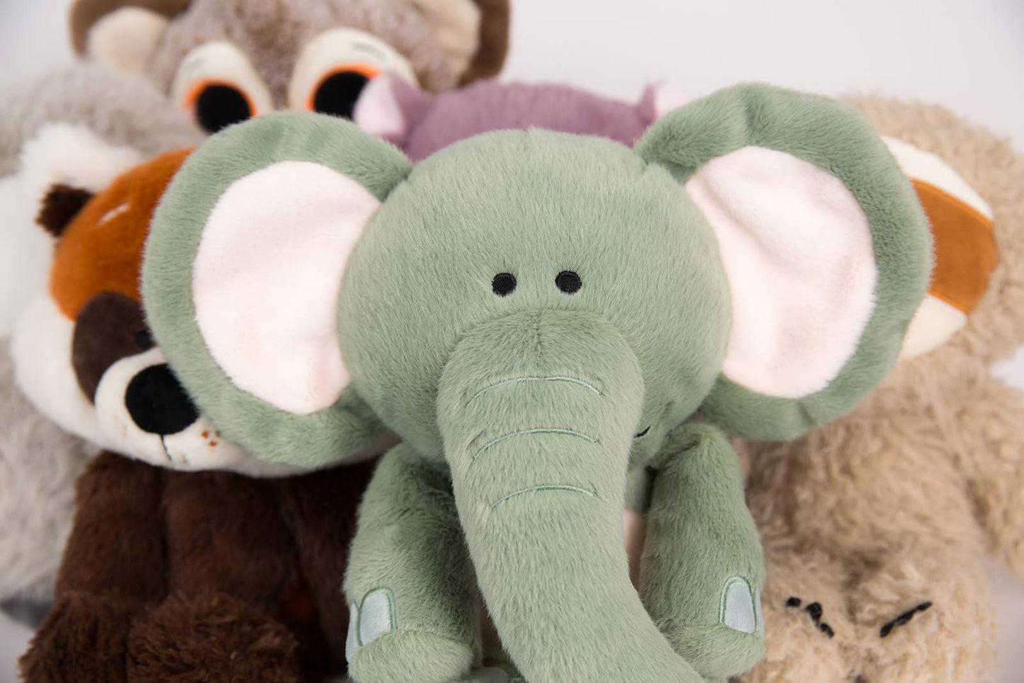 Plush toys including an elephant, raccoon, and bear on a white background