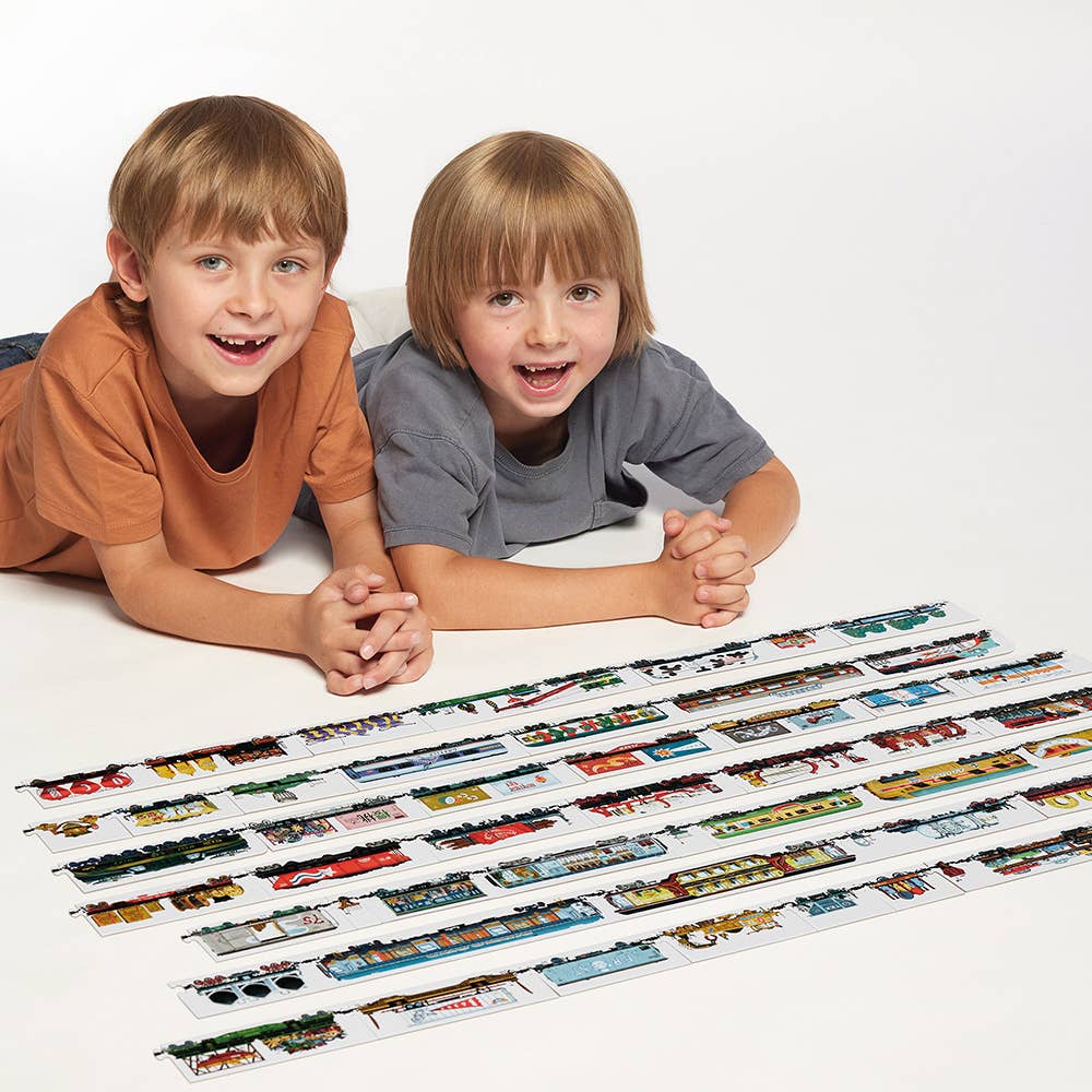 Two children lying on a white surface with a display of toy trains.