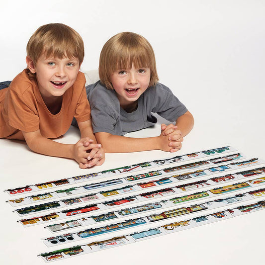 Two children lying on a white surface with a display of toy trains.