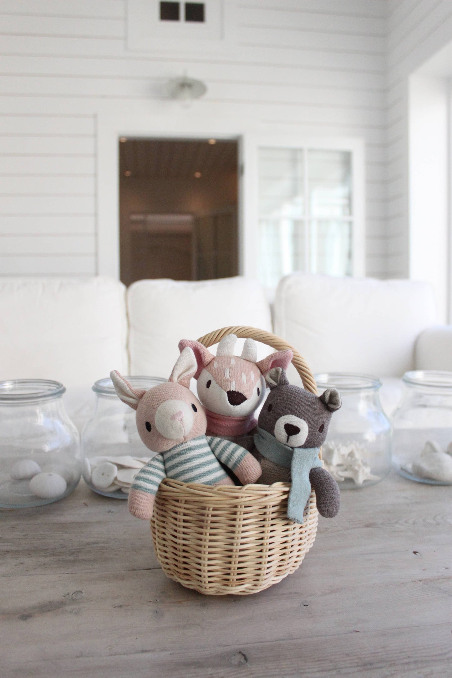Three stuffed animal toys in a woven basket on a wooden floor with a white wall background.