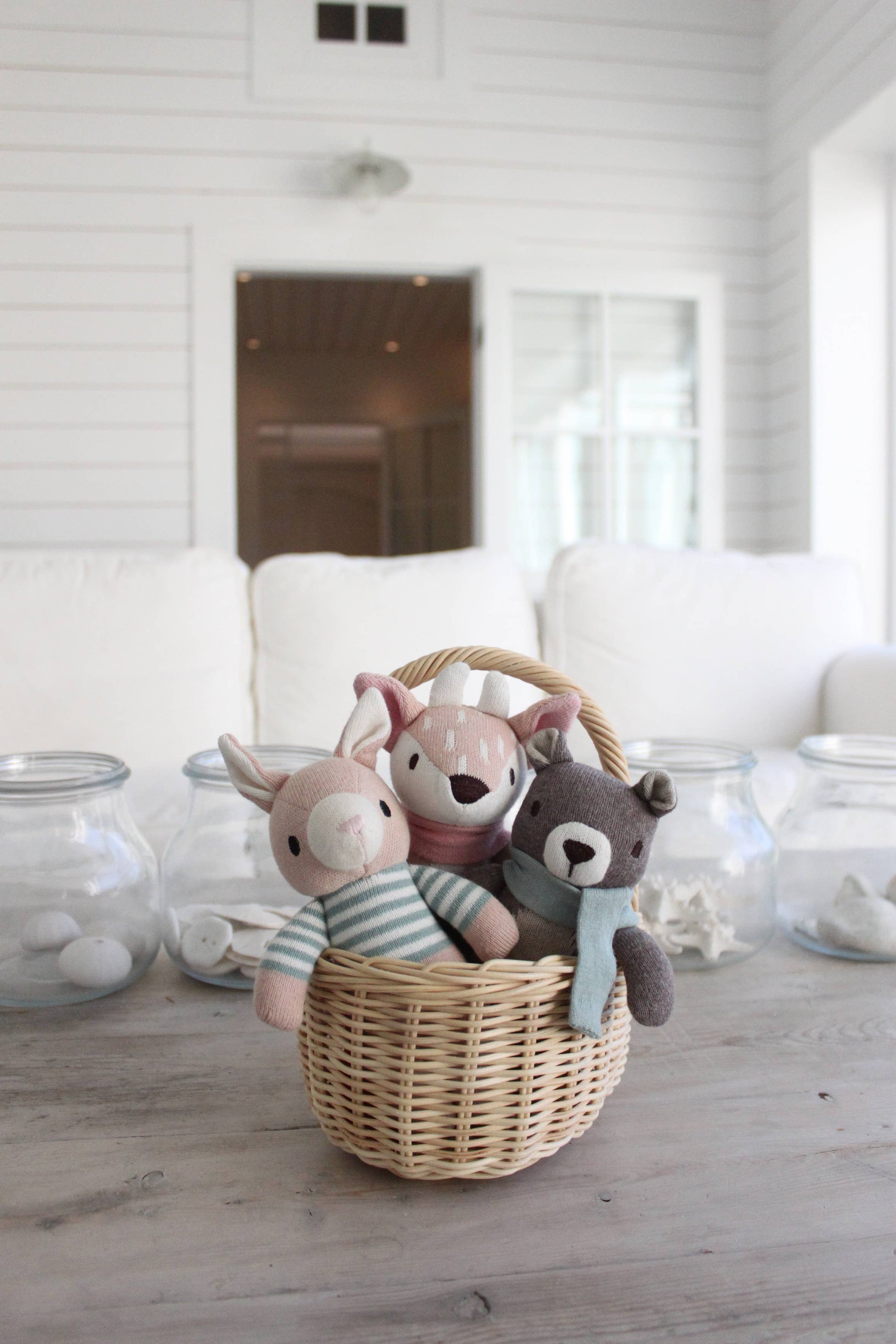 Three stuffed animal toys in a woven basket on a wooden floor with a white wall background.