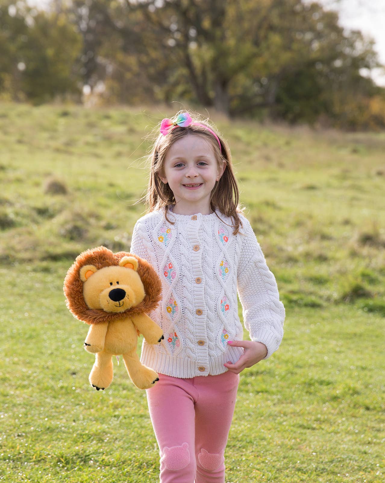 Young girl holding a lion plush toy in a grassy field