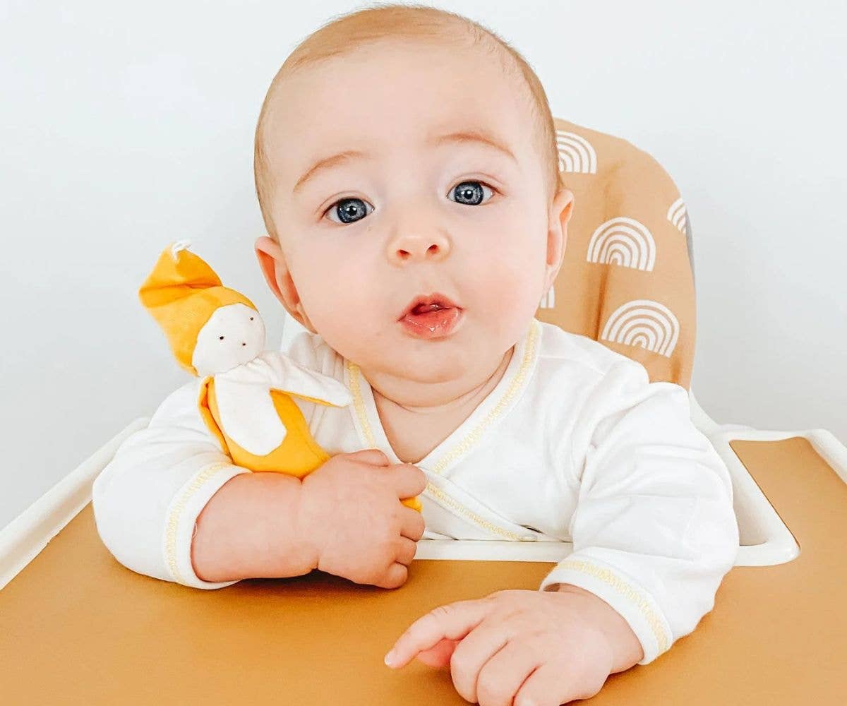 Baby sitting in a high chair with a toy, looking at the camera.