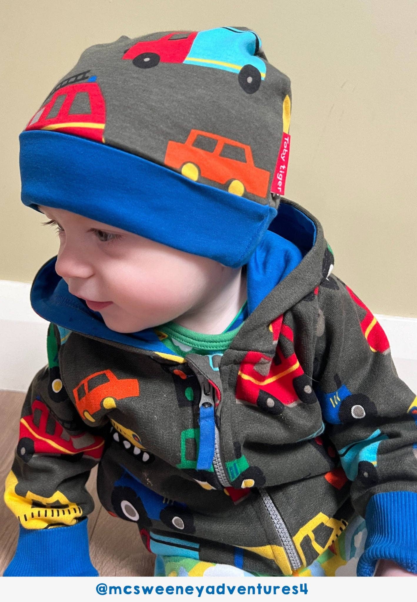 Child wearing a colorful hat and coat with vehicle patterns on a plain background