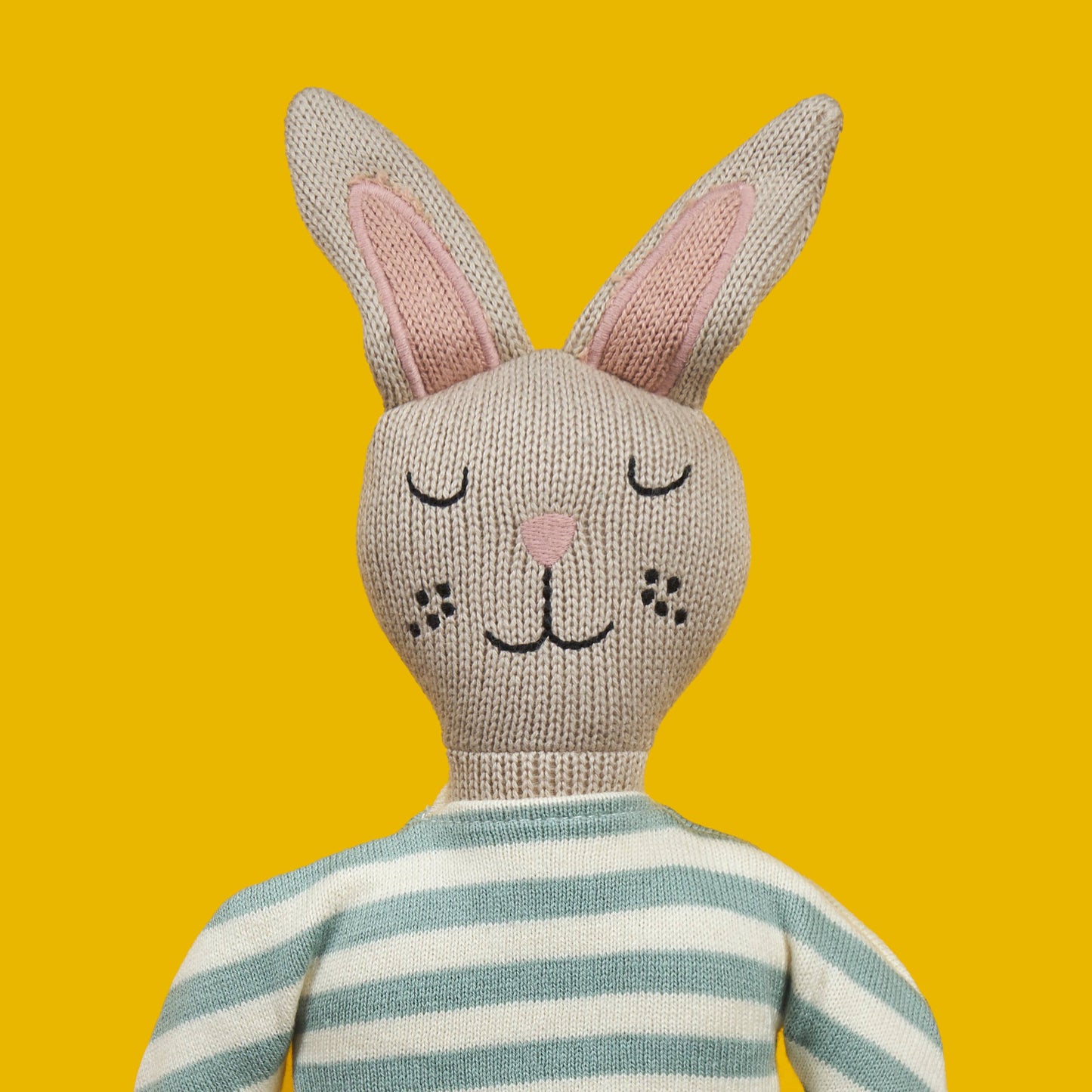 Knitted bunny toy with a striped sweater on a yellow background