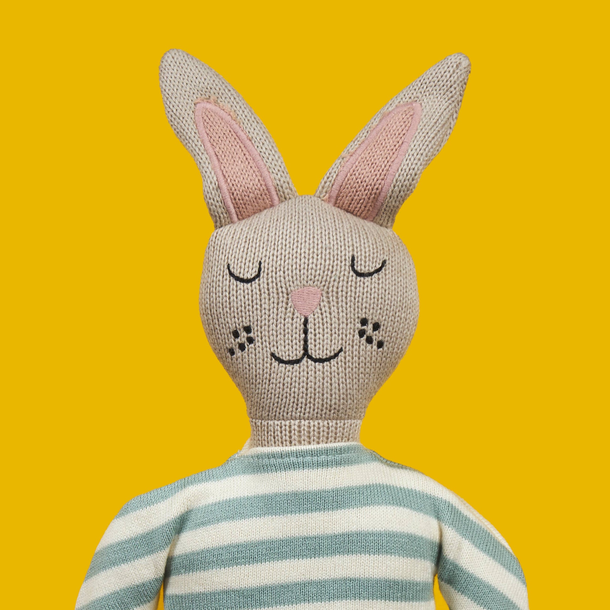 Knitted bunny toy with a striped sweater on a yellow background