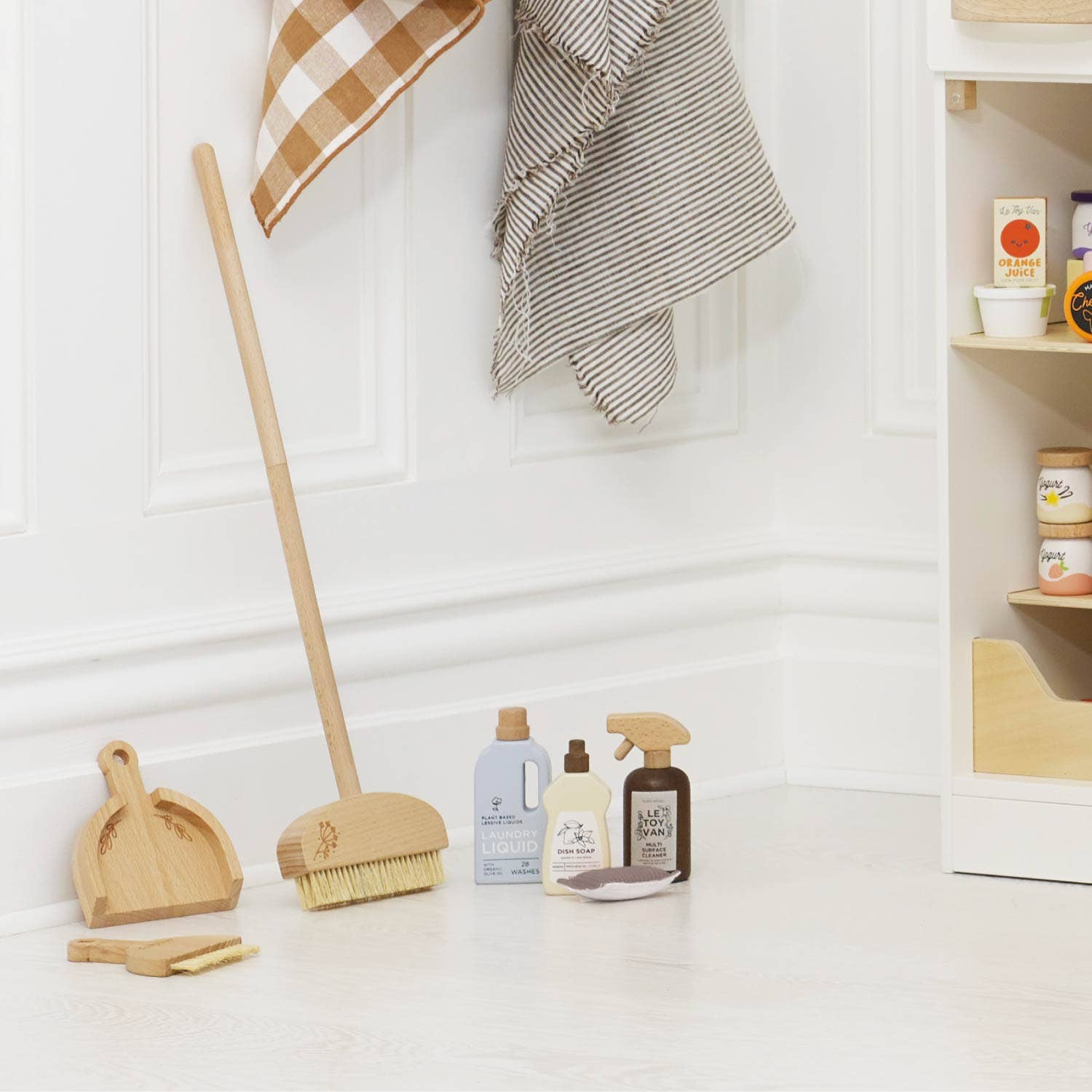 Wooden cleaning toys placed in front of a white door next to a kitchen cupboard