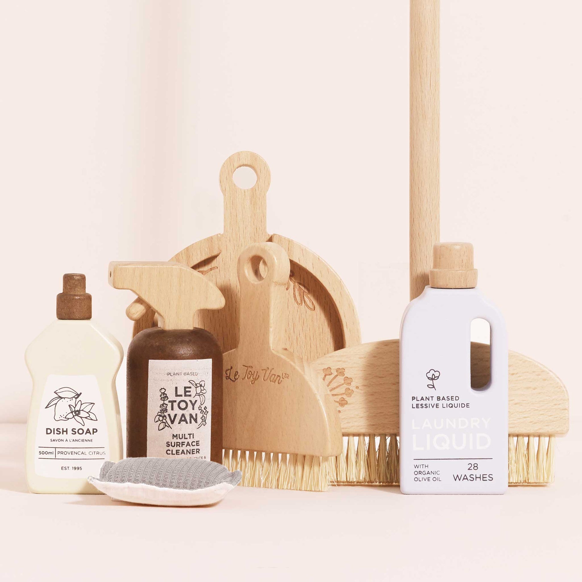 Set of wooden toy cleaning products including bottles, a scrub brush, and a dustpan on a light background