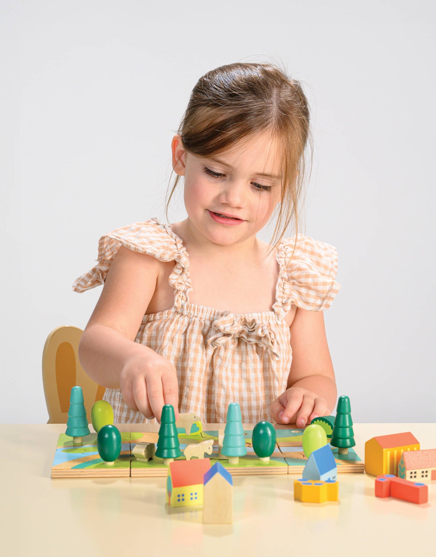 Young girl playing with a wooden toy set on a light surface.