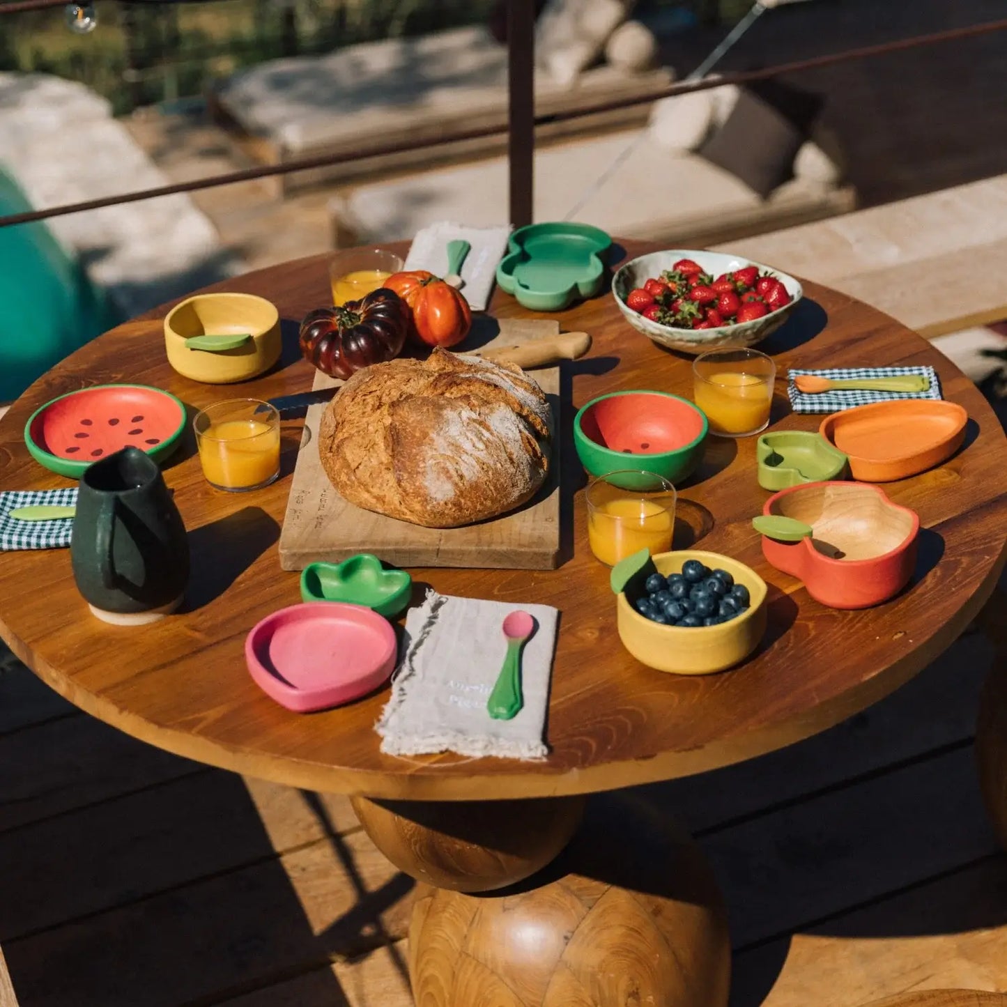 Wooden table with colorful plates, bowls, and food items outdoors.